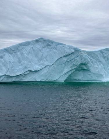 A large iceberg floating in the ocean under a cloudy sky.