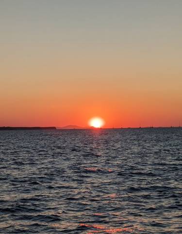 A beautiful sunset over the sea with boats visible on the horizon.
