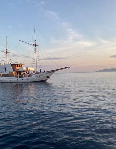 Sailing boat on calm waters at sunset with an island in the distance.