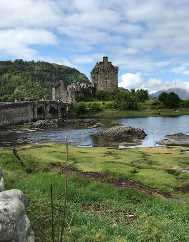 Eilean Donan Castle surrounded by greenery and a stone bridge.