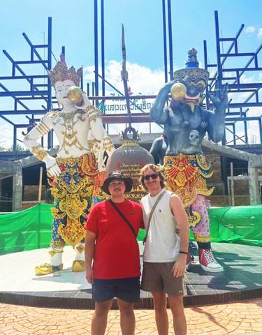Two men posing in front of colorful statues at a temple.