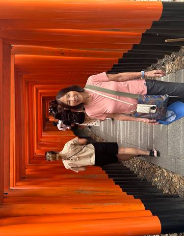 Tourist smiling in a corridor lined with red wooden torii gates.