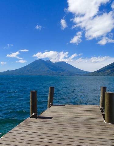 A dock extending into a clear blue lake with mountains.