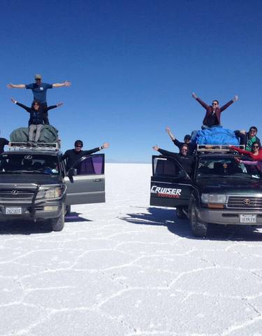Group of people on SUVs in a white salt flat environment.