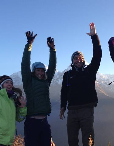 Group of people in winter attire, raising hands joyfully with snowy mountain backdrop.