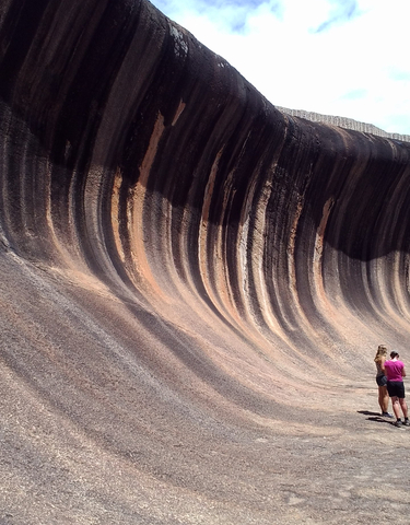 Two people looking at a large, natural wave rock formation.