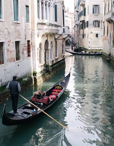A gondola being rowed in a narrow canal with historical buildings.