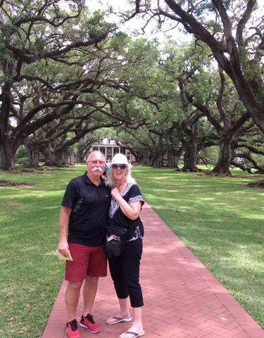 Couple posing under oak trees leading to a house.