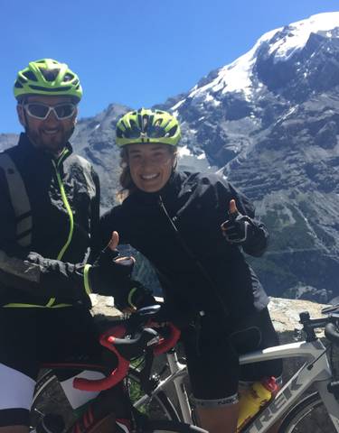 Cyclists posing with thumbs up, snow-capped mountains in the background.