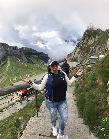 Person posing on a mountaintop with rocky peaks and clouds.