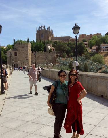 People standing on a stone bridge with a historic city in the background.