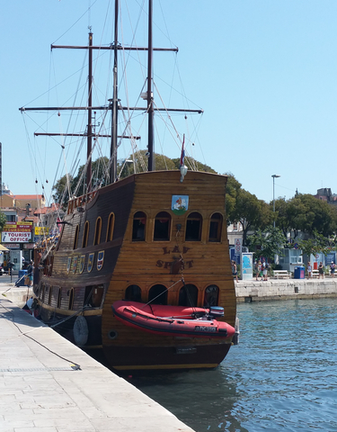 Wooden ship docked near waterfront with excursion signs.