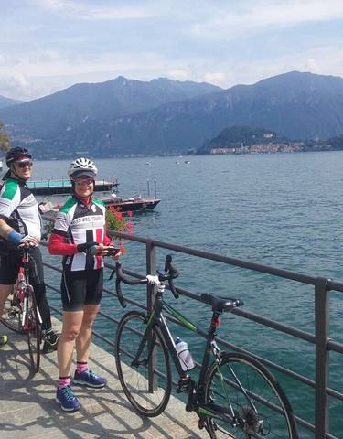 Two cyclists posing by a lake with mountains in the background.
