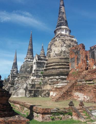 Ancient temple ruins with large stupas under a bright blue sky.