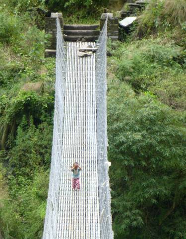 Person crossing a long suspension bridge in a forested area.