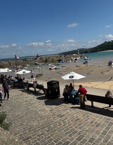 Harbor with boats and people sitting on a bench with an umbrella and stone pavement.