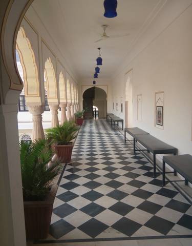 An interior view of a corridor with checkerboard flooring and potted plants.