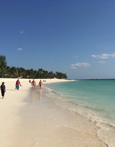 Beach with people walking and boats in the water.