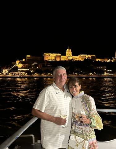 A couple posing with an illuminated building in the background at night.