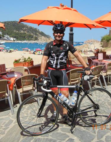 Cyclist posing with a bicycle by the beach with umbrellas in the background.