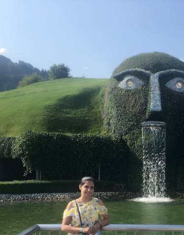 Large grass-covered sculpture with a fountain, woman posing in front.