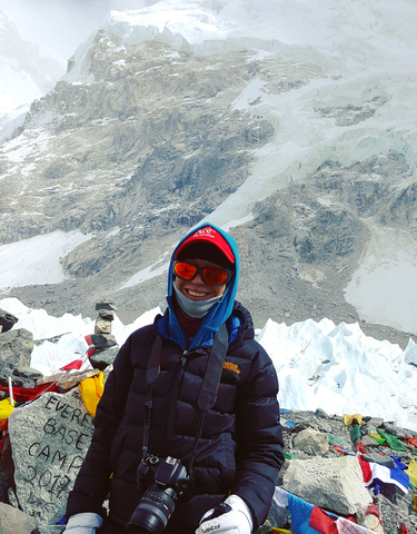 Person with trekking gear posing with snowy mountains in the background.