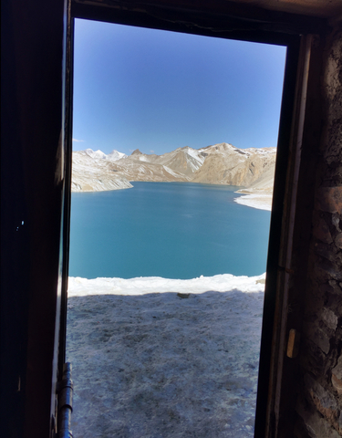 Scenic view of a blue lake surrounded by mountains, viewed from a doorway.