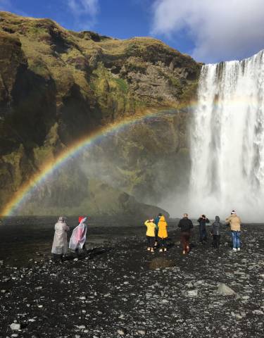 Waterfall with a rainbow viewed by spectators in rain gear.