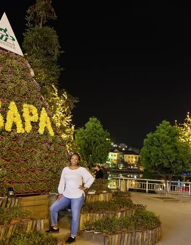 A person posing in front of a Sapa sign made of plants, lit at night.