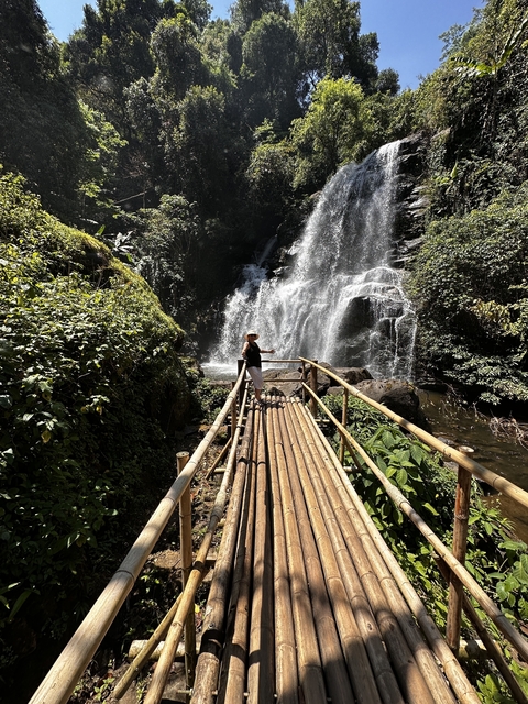 Person standing on a wooden bridge near a waterfall.