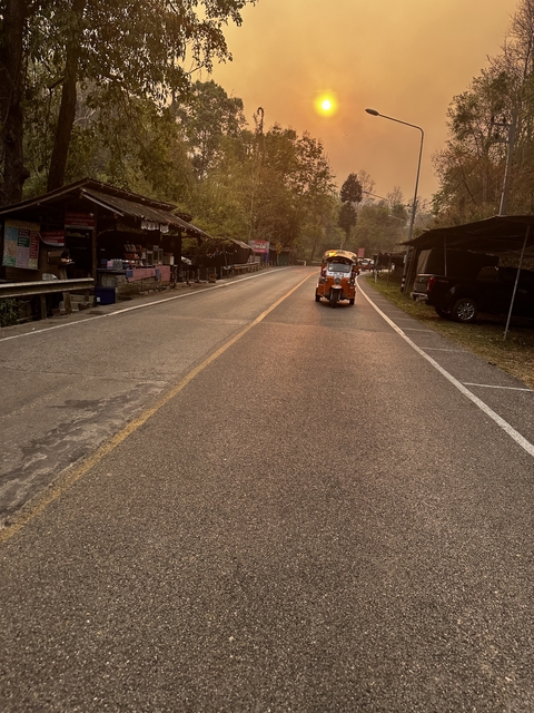 A tuk-tuk on a road lined with shops in the early evening.