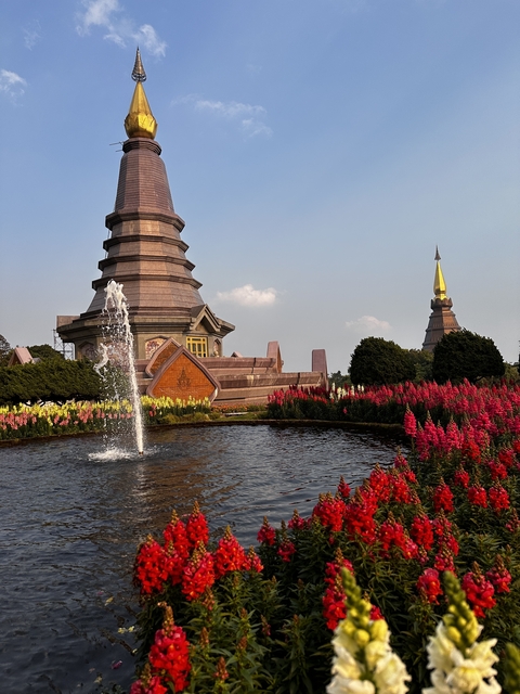Garden with a fountain and stupas, surrounded by flowers.