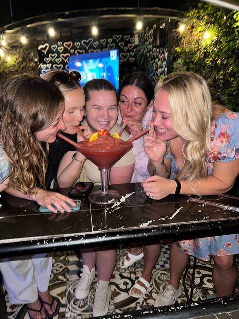 Group of people enjoying a large cocktail at a table.