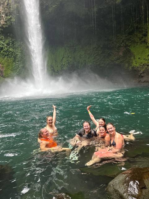 A group of people swimming at the base of a waterfall.