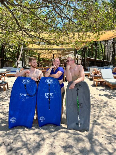 Three people posing with bodyboards on a beach.