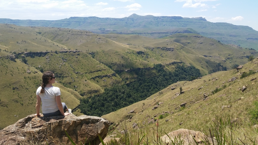 A person sitting atop a rock overlooking a vast valley.