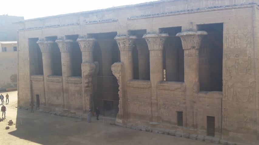 Ancient building with columns and people walking.