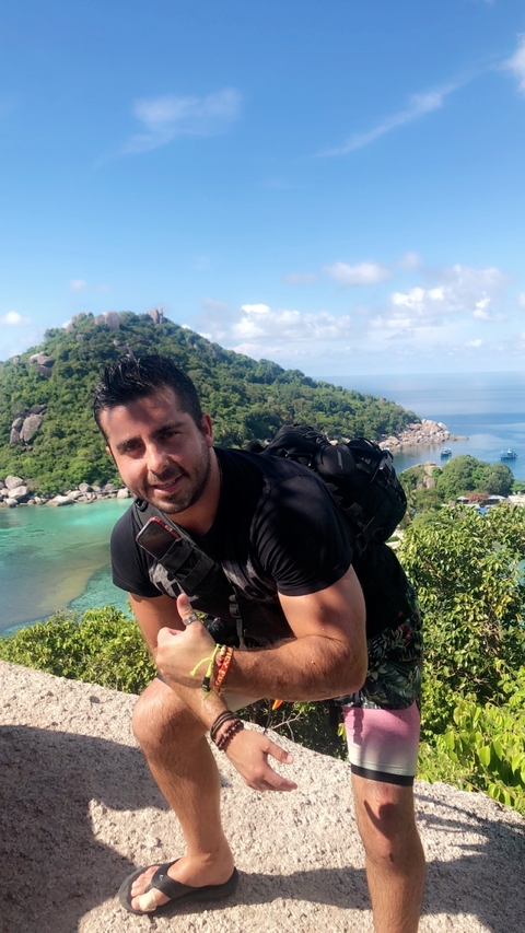 Person posing with a lush green island and blue sea in the background.