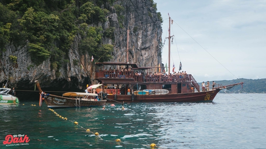 Wooden boats with people swimming in clear ocean water.