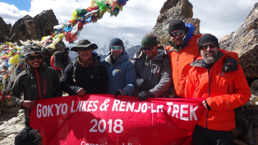 Group of trekkers holding a banner with snow-capped mountains in the background.