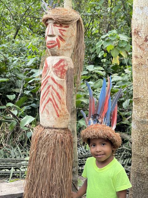 Child standing by a carved statue with feathers.