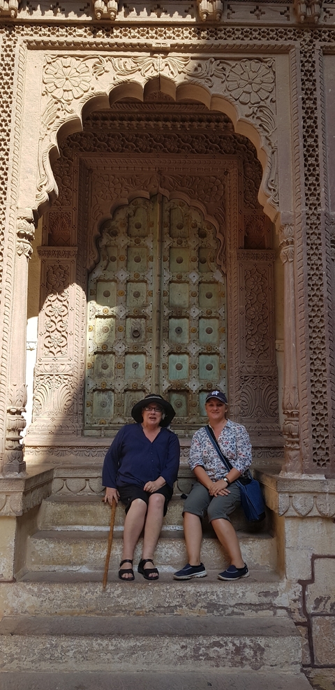 Two women posing in front of a large, ornate door.