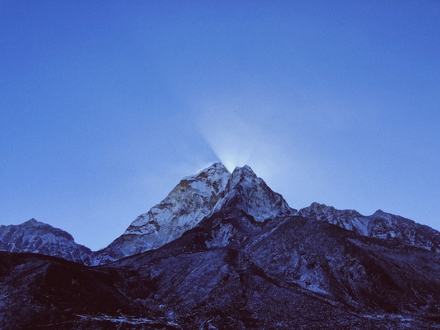 Mountain peaks with sunlight rays emerging from the top.