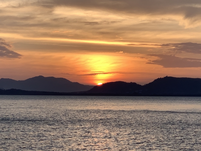 Sunset over the ocean with silhouetted mountains.