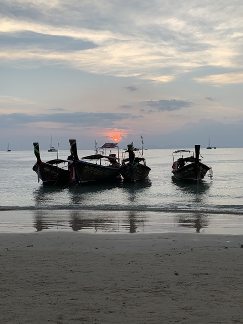 Longtail boats near the shore with a sunset backdrop.