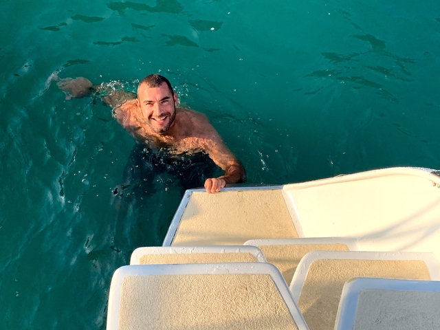 Man swimming in clear water next to a boat.