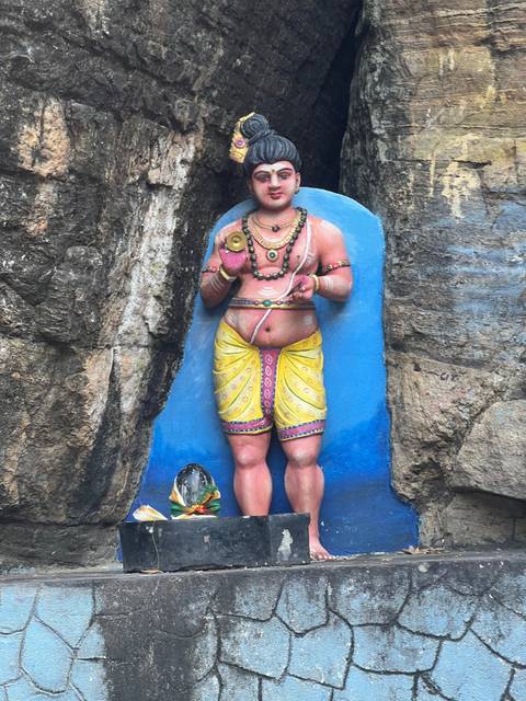 A colorful statue of a figure holding an object, placed against a rock wall.