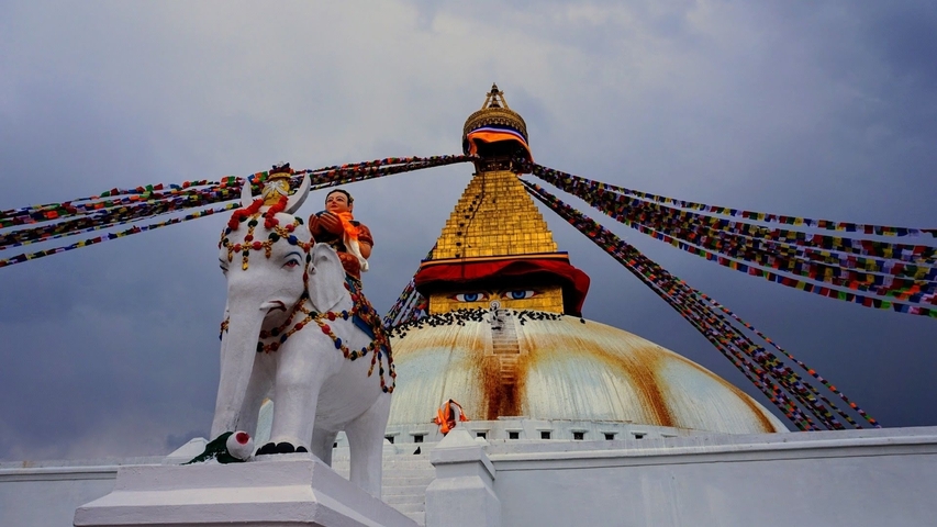 A stupa with prayer flags and a statue of an elephant in a religious site.