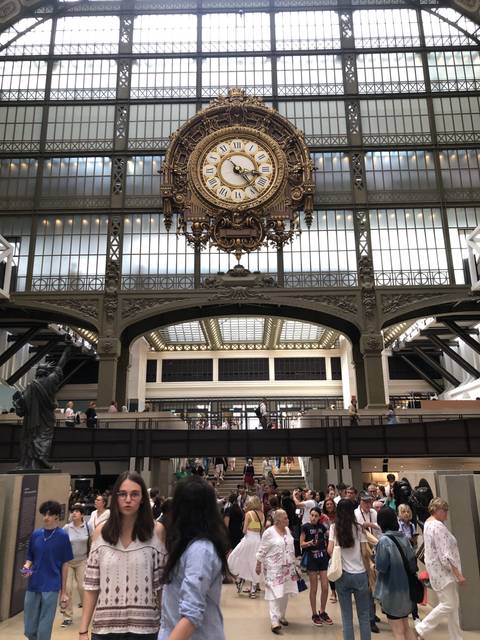 A large ornate clock inside a crowded gallery or museum space.