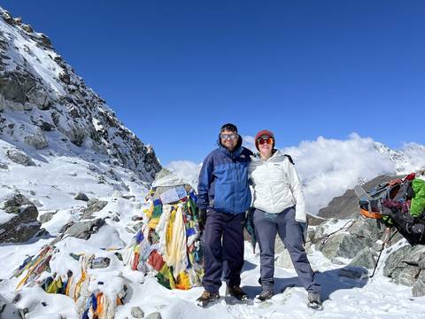 Hikers at the summit of a snow-capped mountain with prayer flags.